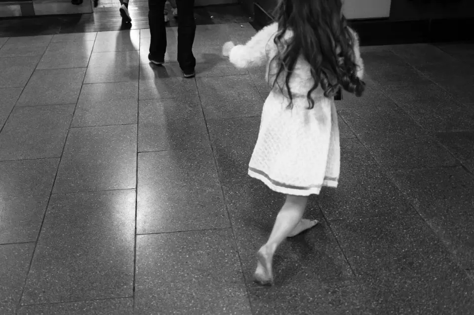 Lyrical image of a young, barefoot girl in a white dress running on the tiled floor near a tube escalator