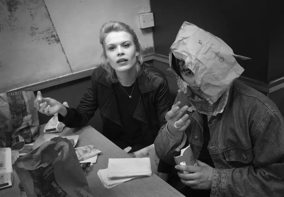 A striking young woman and her male companion eat at a table in Macdonalds, he has a paper bag covering most of his head and face