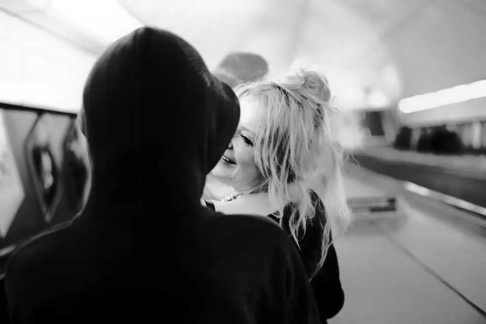 Woman smiles at dark, hooded figure on tube escalator 