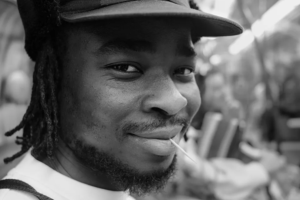 Close shot of a confidently smiling young man in a tube carriage, a wooden toothpick between his lips