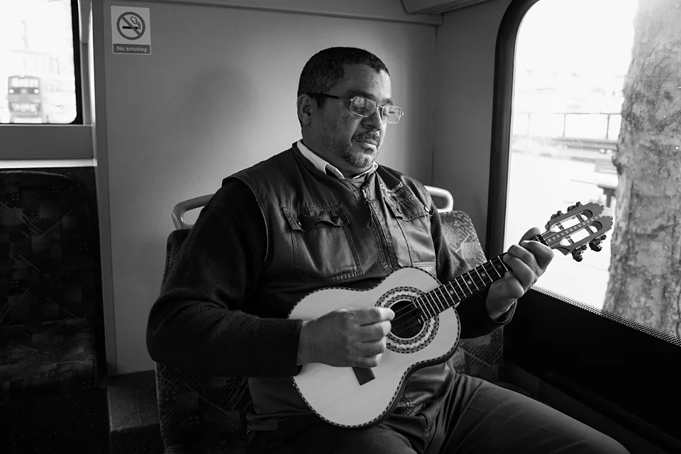 A bus driver sits in the rear of his bus strumming a small guitar during his work break