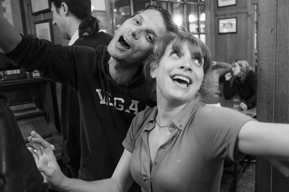 A young man and woman sing along happily to a song played on the pub piano 